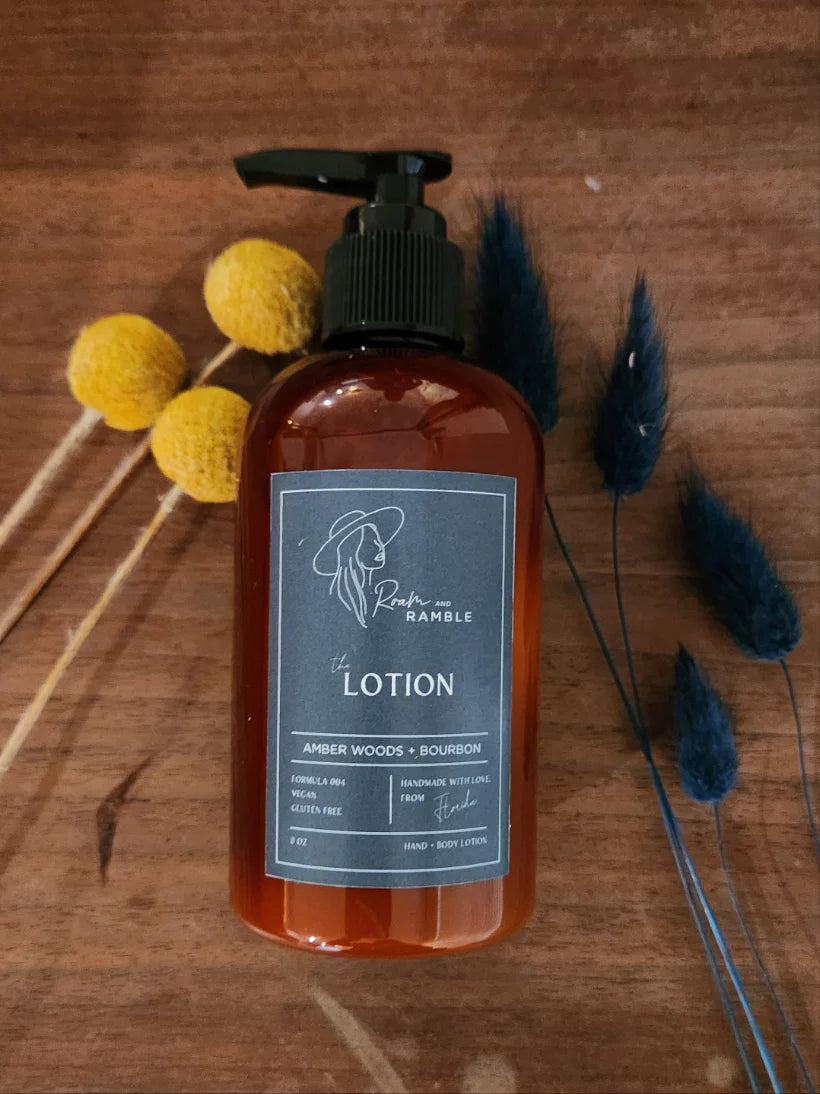 Amber Woods & Bourbon Lotion laying on a wood surface with dried florals.