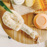 Baudelaire Sisal Bath Brush, shown laying on wooden table with a bar of soap.