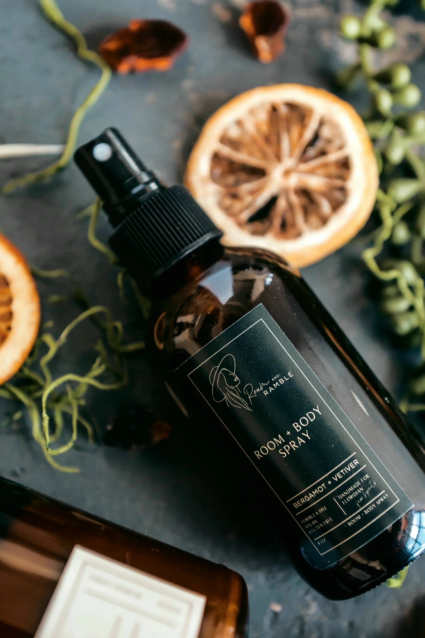 Room and body spray bottle with dried oranges and greenery on a dark surface