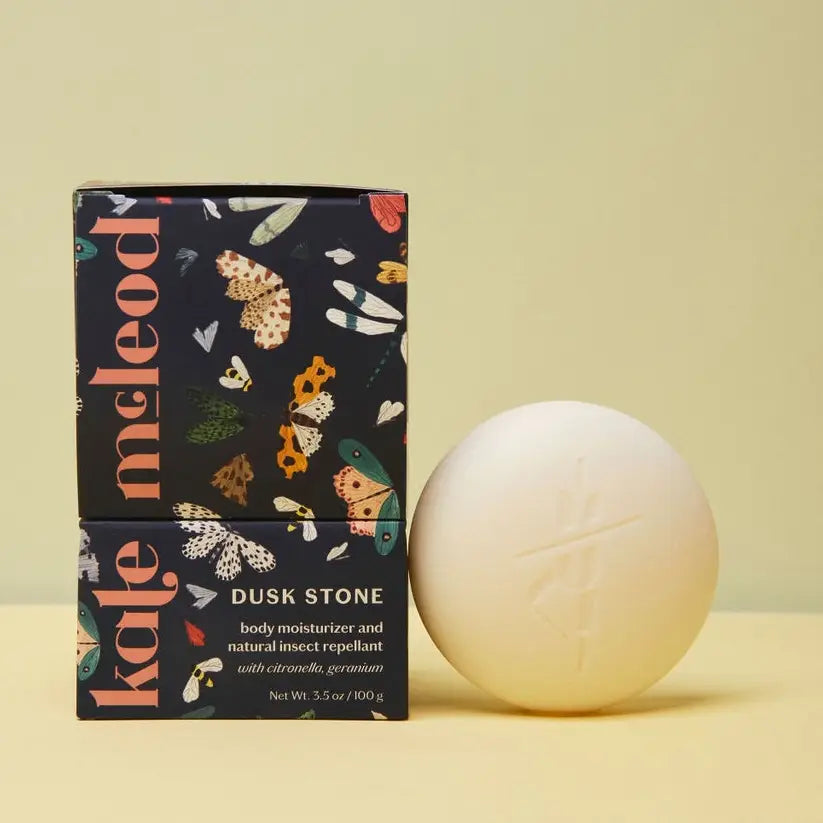 Kale Meleod body moisturizer and natural insect repellant packaging with a white stone on a yellow background