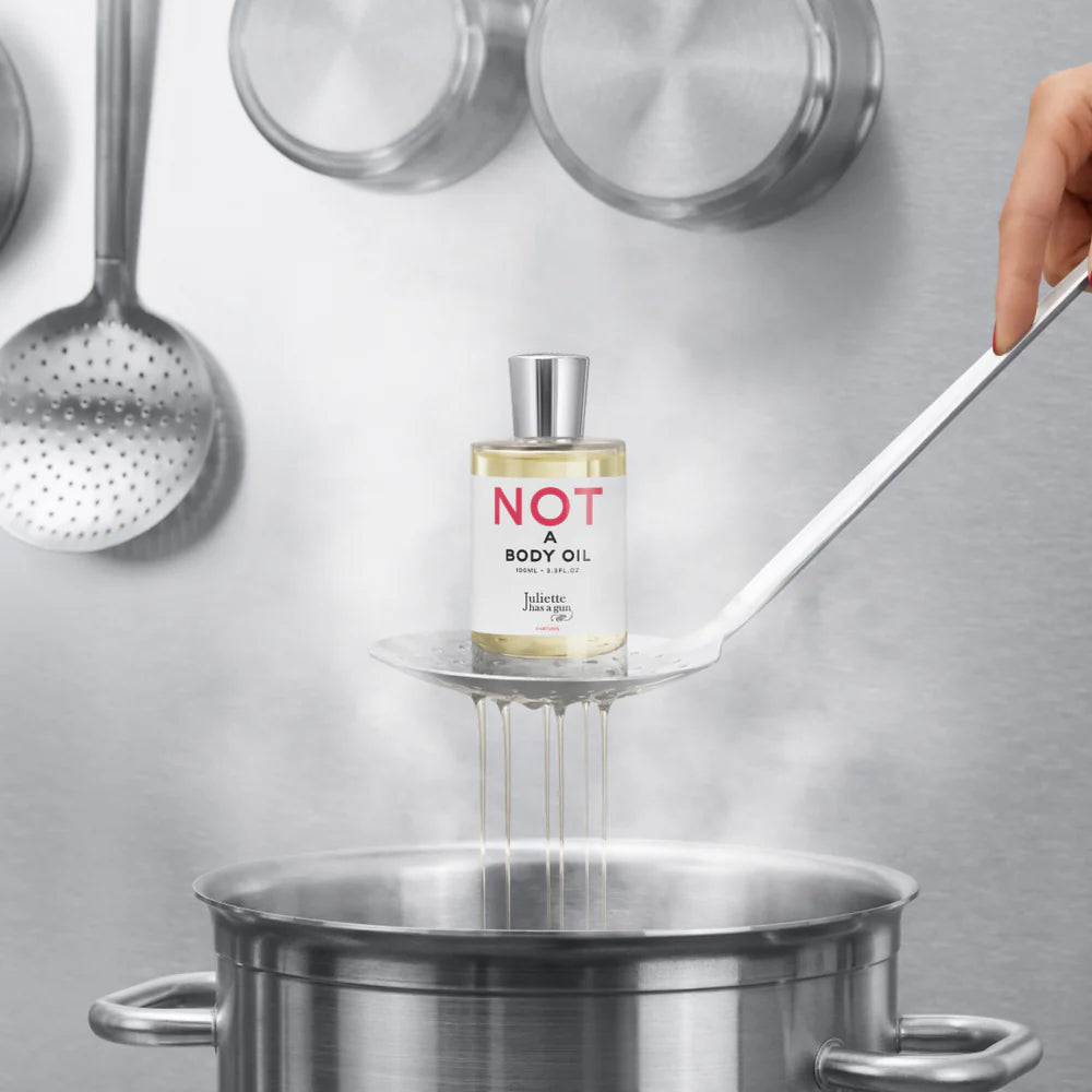 Juliette Has a Gun Not A Body Oil 100mL, available at Rafa Natural. Hand holding ladle over pot, with product in the ladle.