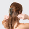 Woman wearing light green hair clip while holding hands up.