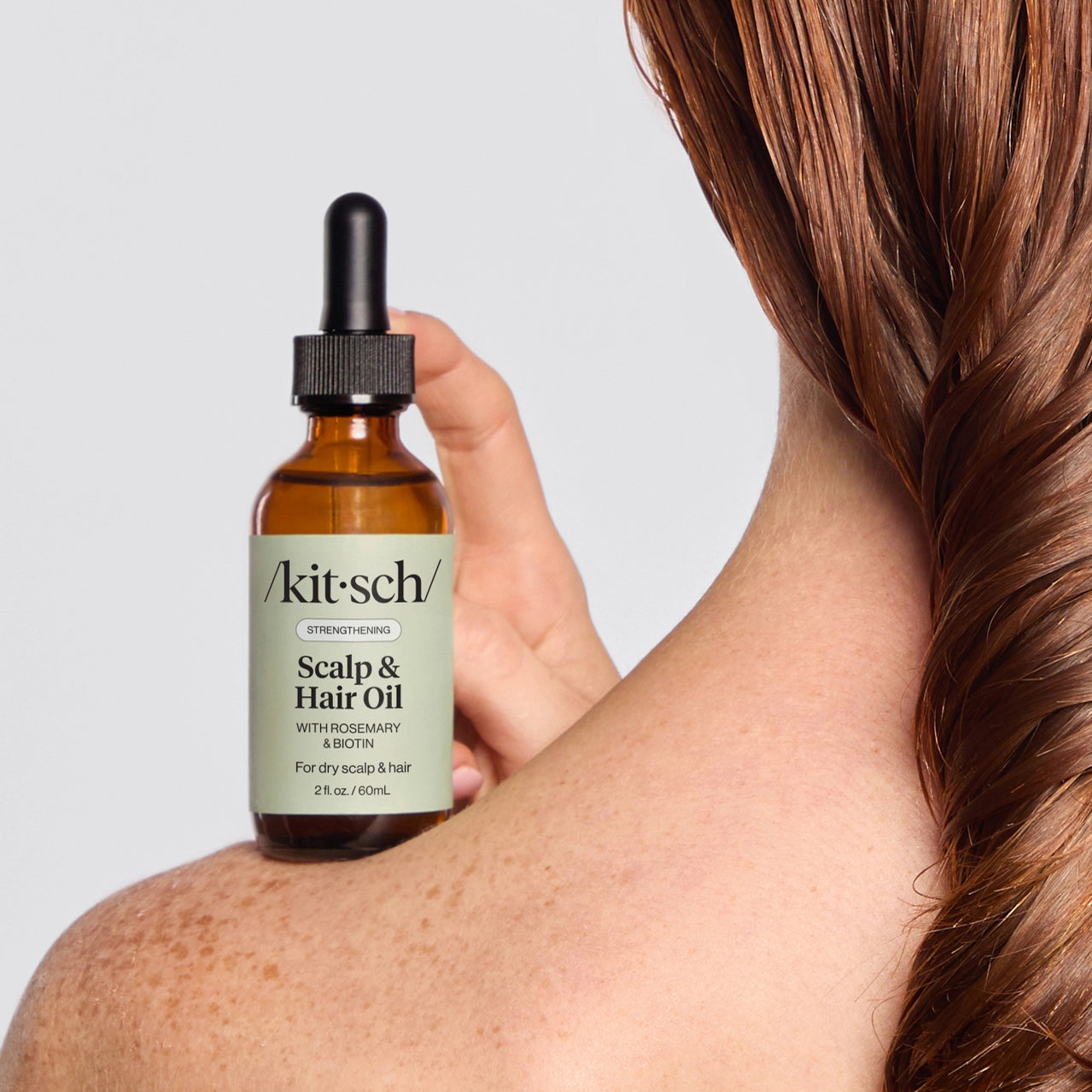 Person holding a bottle of 'Kitsch' scalp and hair oil with a neutral background