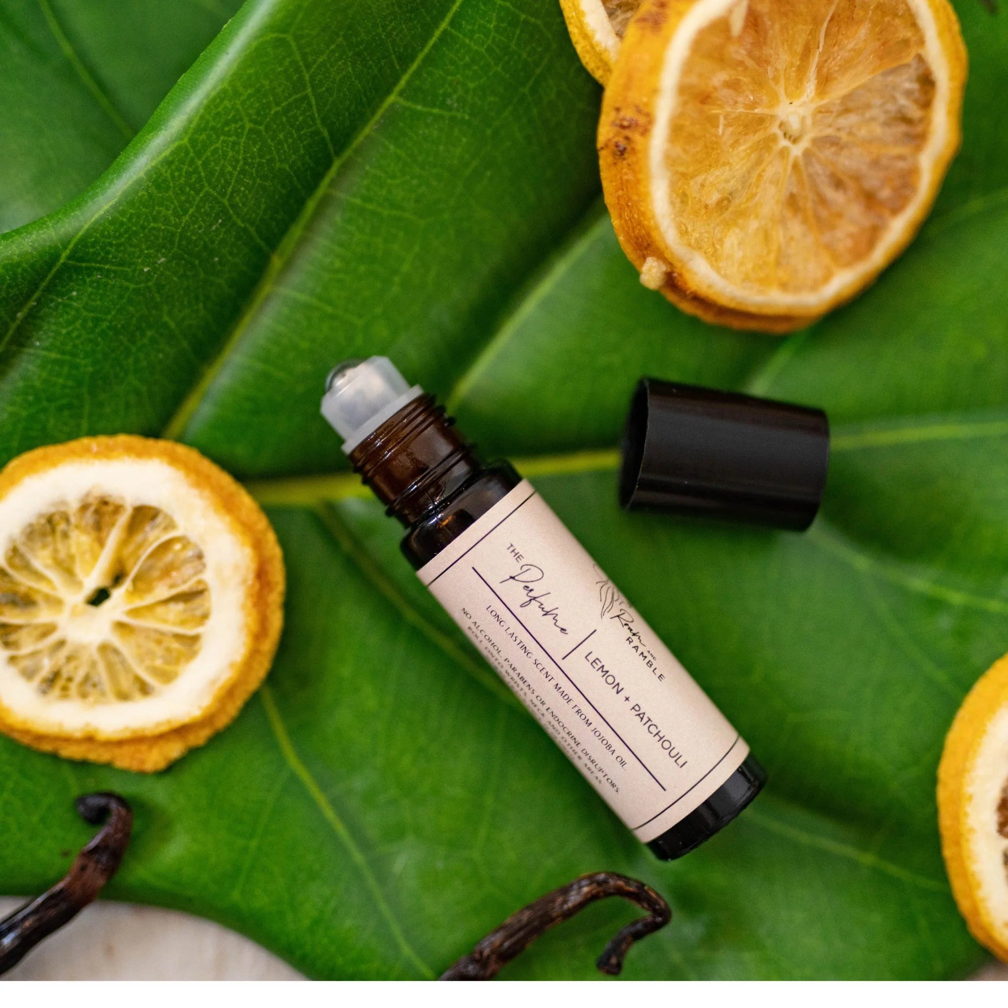 Roll-on bottle with a beige label on green leaves with dried oranges and vanilla beans.