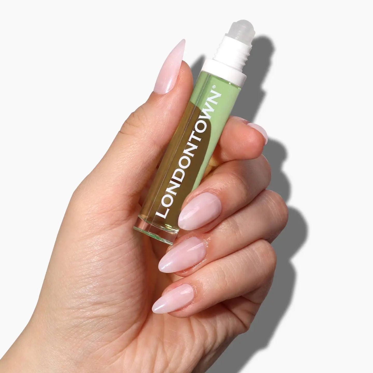 Hand holding Londontown Agave Pear Roll & Glow Cuticle Oil with rollerball applicator against white background
