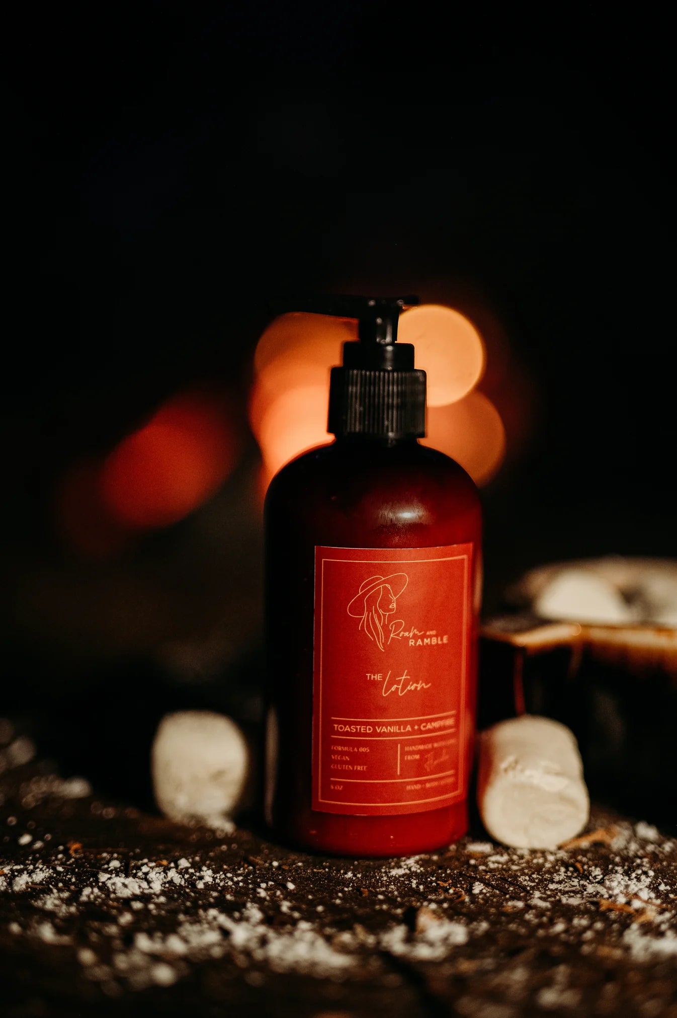 Roam and Ramble Toasted Vanilla Campfire Lotion on dark surface with marshmallows.