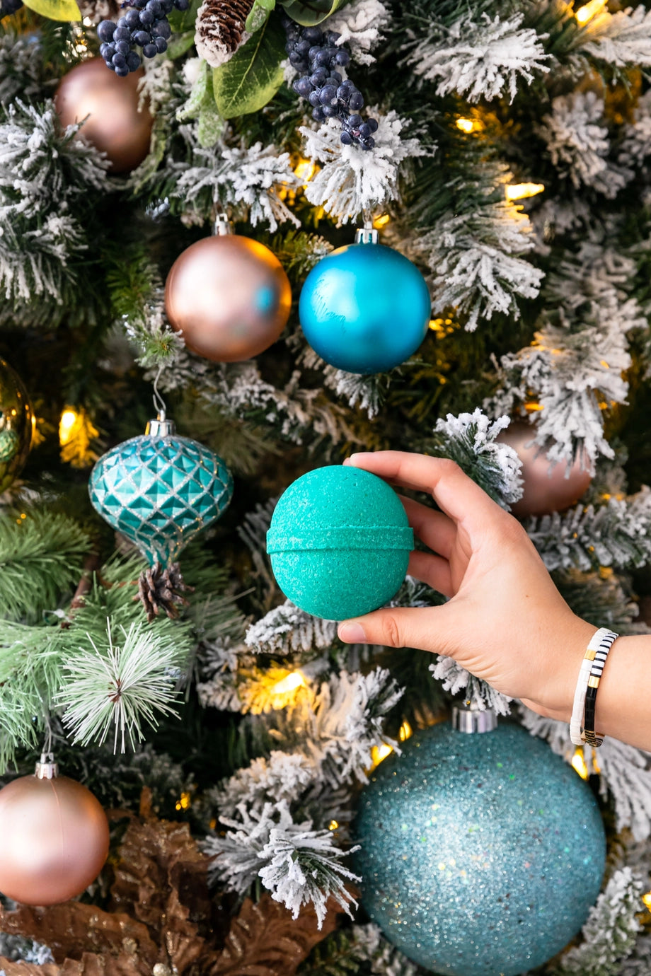 Hand holding a turquoise ornament against a Christmas tree with colorful ornaments.