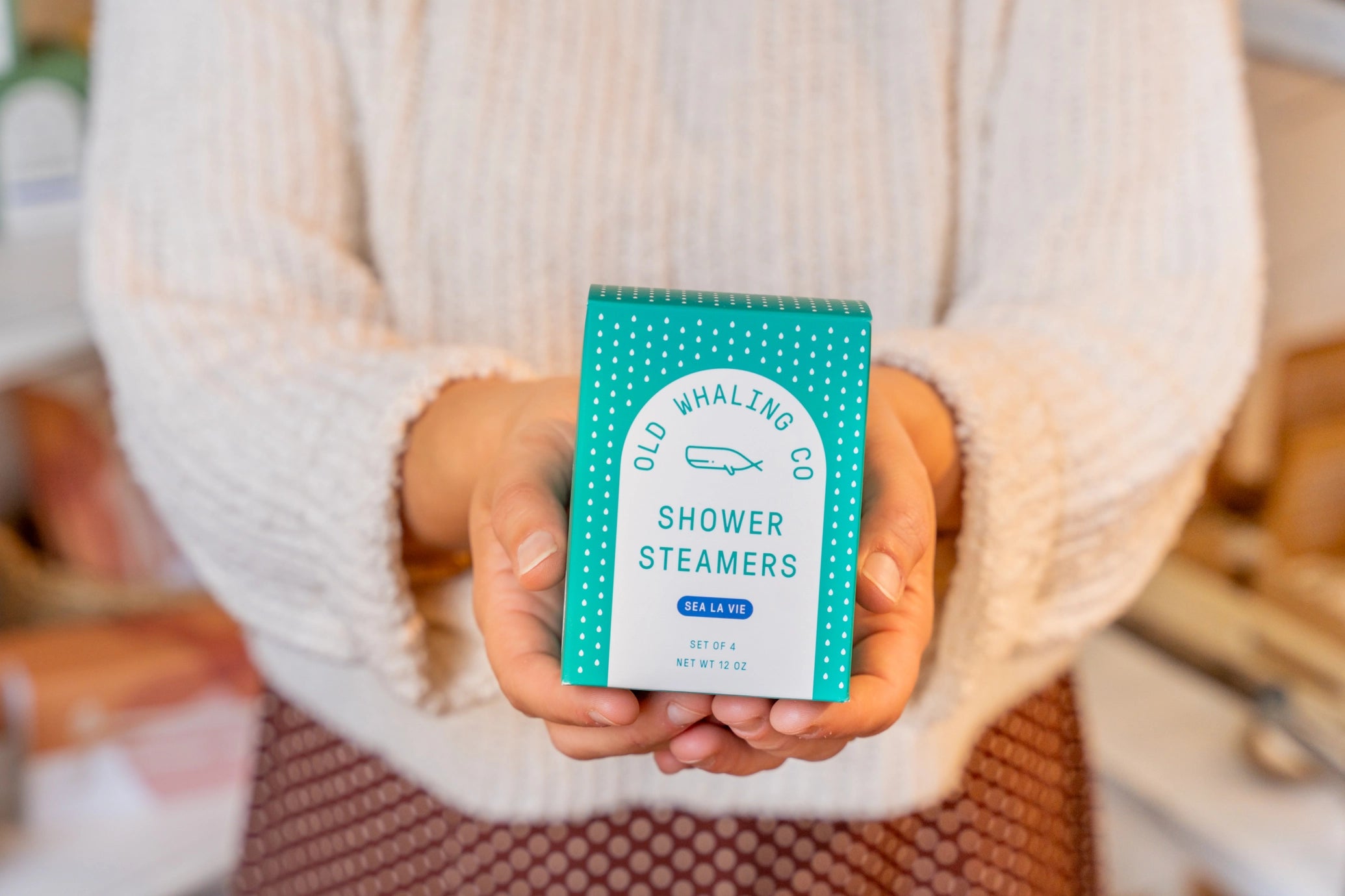Person holding a box of Old Whaling Co. Shower Steamers in a cozy indoor setting.
