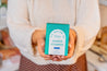 Person holding a box of Old Whaling Co. Shower Steamers in a cozy indoor setting.