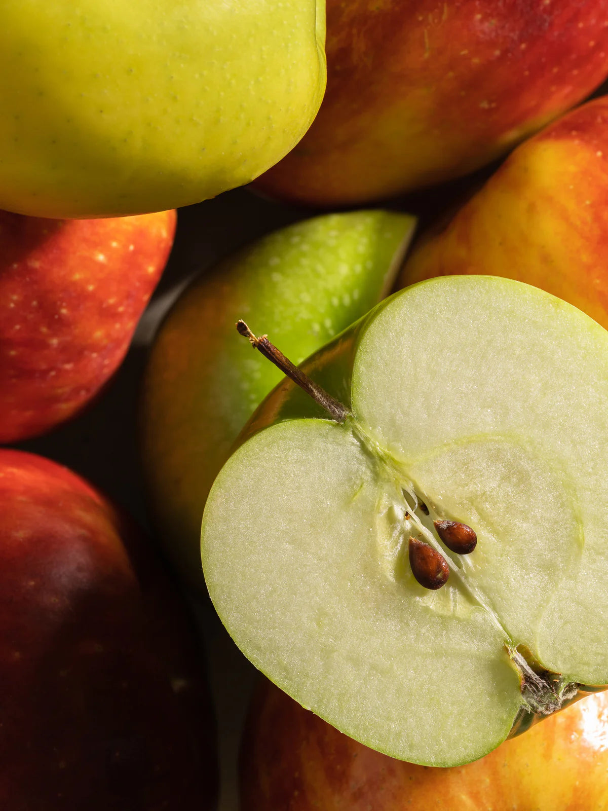 Close-up of green and red apples with a halved apple showing seeds.
