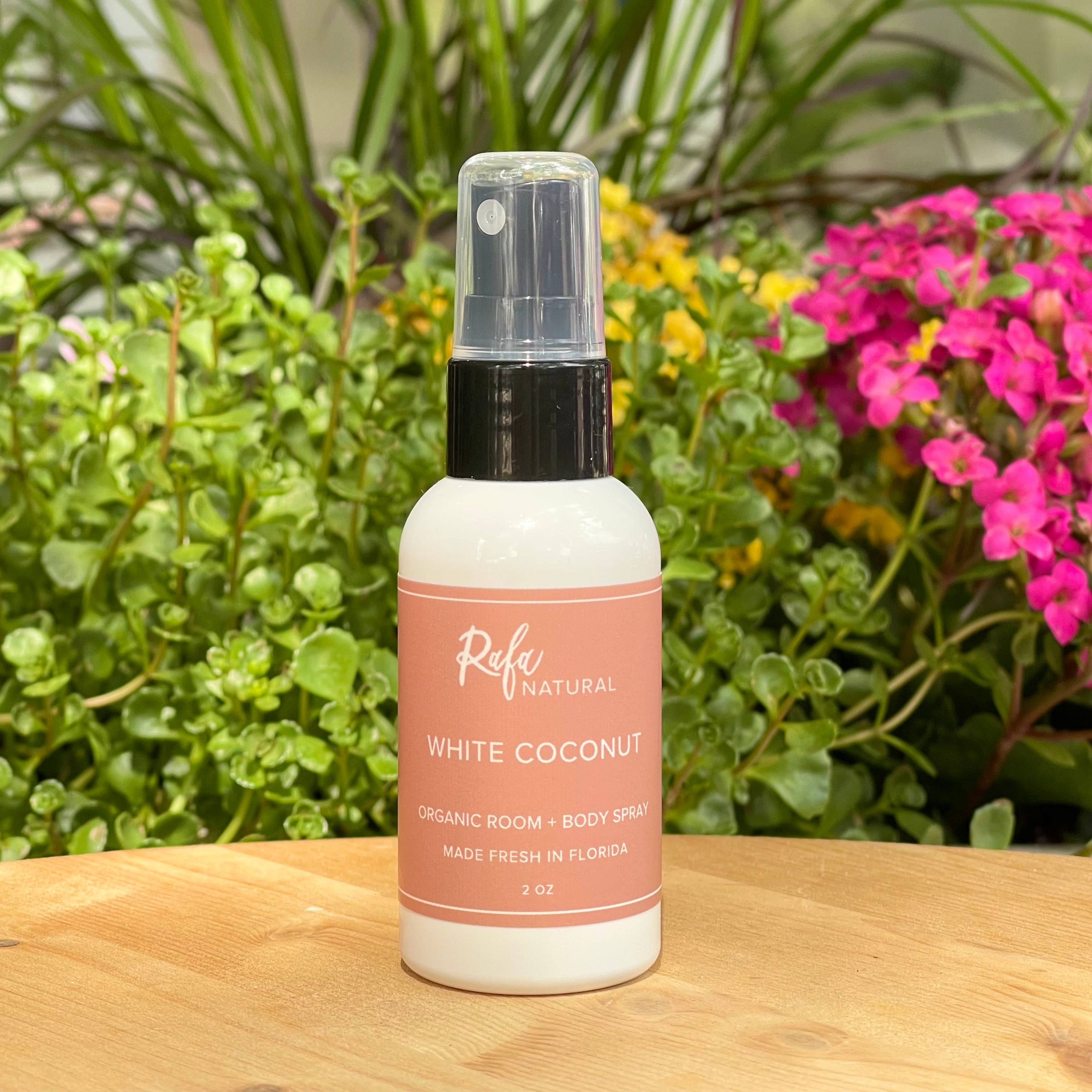 White Coconut 2oz Room & Body Spray, on wood table, with greenery in background.